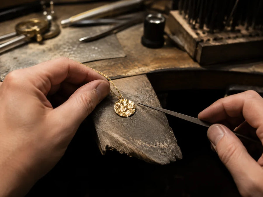 Goldschmied verarbeitet einen Berg-Anhänger aus Fairmined-Gold von Hand an der Werkbank